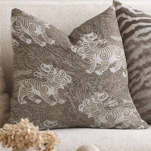 May include: A collection of decorative throw pillows in various patterns and colors. Two pillows feature detailed patterns, one with a tiger-like design and the other with a repeating motif of mythical creatures. A solid brown pillow and a cream-colored pillow are also visible.