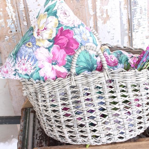 Puede incluir: Una cesta de mimbre blanca con un forro de tela con estampado floral y una almohada floral en su interior. La cesta tiene un asa y est&aacute; llena de ramitas de lavanda.
