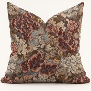 May include: A square throw pillow featuring a dense, woven tapestry pattern of stylized leaves and floral shapes. The fabric displays a rich color palette of deep burgundy, muted brown, soft beige, and slate blue tones throughout the design.
