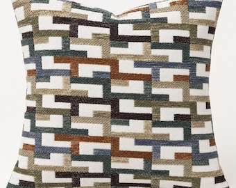 May include: A square throw pillow featuring a textured geometric pattern of interlocking rectangular shapes. The design incorporates a color palette of white, dark brown, muted olive green, slate blue, and tan, creating a repeating mosaic effect.