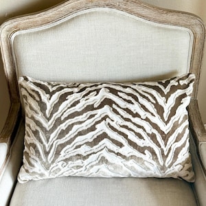 May include: A brown and white zebra patterned throw pillow on a light beige armchair.
