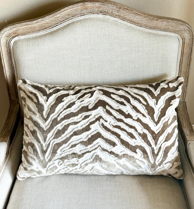 May include: A brown and white zebra patterned throw pillow on a light beige armchair.