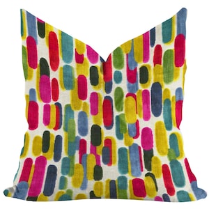 May include: A decorative throw pillow with a colorful abstract design. The pillow features a pattern of vertical, oblong shapes in various colors, including yellow, pink, blue, green, and black, set against a cream-colored background. The pillow has a soft, textured appearance.