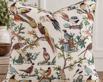 May include: A square throw pillow featuring a cream-colored fabric base with a repeating pattern of colorful pheasants, birds, and foliage. The design includes various birds in shades of brown, orange, blue, and yellow perched on branches.