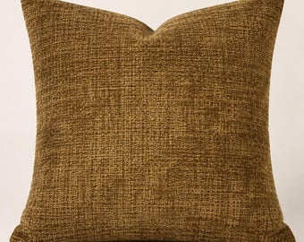 May include: A square throw pillow featuring a textured, woven fabric in a deep mustard yellow or ochre tone. The material displays a consistent, dense grid-like pattern with subtle variations in color depth across the entire surface area.