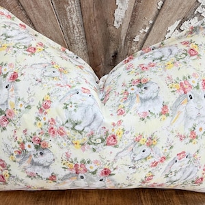 Könnte beinhalten: Ein gelbes Kissen mit einem Blumenmuster mit Hasen und Blumen. Das Kissen ist aus einem weichen, bequemen Stoff gefertigt und perfekt, um Ihrem Zuhause einen Hauch von Frühling zu verleihen.