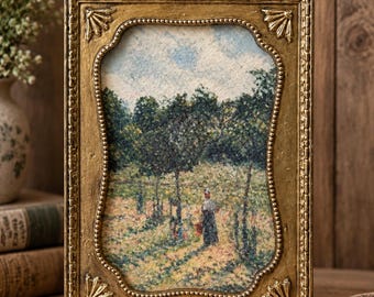 May include: A rectangular gold-toned picture frame with an ornate bow detail at the top and shell-like accents at the corners. The frame holds a textured print depicting a landscape scene with trees, a blue sky, and a figure standing in a field.