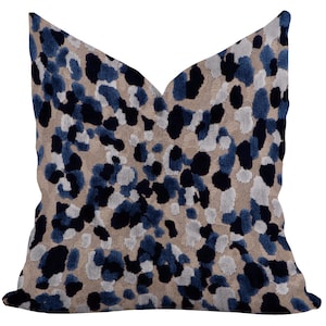 May include: A decorative throw pillow with a beige background and a pattern of navy blue and gray spots. The pillow has a V-shaped design and is made of a soft, textured fabric.