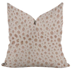 May include: A decorative throw pillow with a beige background and a pattern of brown, irregular spots. The pillow has a soft, textured appearance, and the spots vary in size and density across the surface. The pillow is designed to add a touch of style to any room.