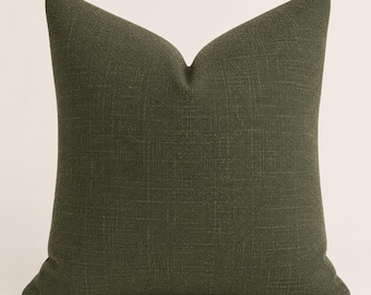 May include: A square throw pillow cover in a solid dark olive green color. The fabric features a visible woven texture with a cross-hatch pattern throughout. The pillow is plumped to create a distinct peak at the top center, showcasing its shape.