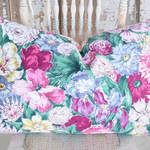 Puede incluir: Una almohada floral con fondo verde y flores rosas, blancas y azules. La almohada est&aacute; hecha de tela y tiene una cremallera.