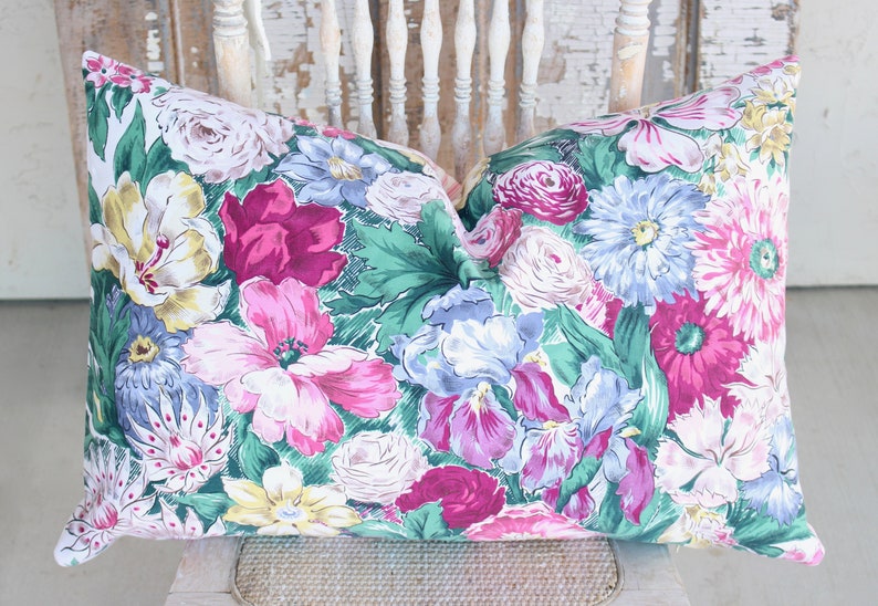 Puede incluir: Una almohada floral con fondo verde y flores rosas, blancas y azules. La almohada est&aacute; hecha de tela y tiene una cremallera.