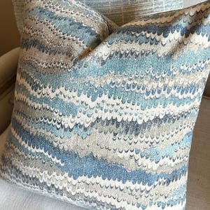 May include: A blue and gray patterned throw pillow with a wavy design. The pillow is made of a soft, textured fabric.