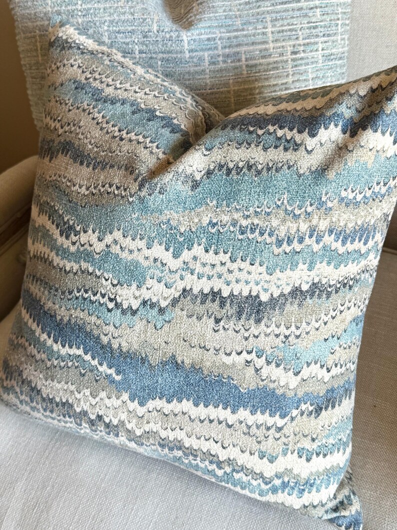 May include: A blue and gray patterned throw pillow with a wavy design. The pillow is made of a soft, textured fabric.