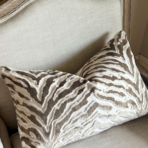 May include: Two decorative throw pillows with a brown and white zebra print pattern. The pillows are on a light beige armchair.