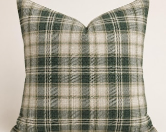 May include: A square throw pillow featuring a classic plaid pattern in shades of forest green, olive, and cream. The fabric has a visible woven texture, and the design consists of intersecting horizontal and vertical lines forming a grid.