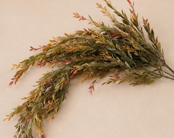 May include: A decorative artificial plant spray featuring slender, cascading stems covered in small, pointed leaves. The foliage displays a gradient of colors, transitioning from deep forest green to warm golden yellow and hints of reddish-orange.