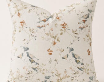 May include: A square throw pillow featuring an off-white base fabric with a delicate watercolor-style botanical print. The pattern consists of thin, branching stems with small leaves in muted shades of sage green, dusty blue, and burnt orange.