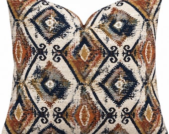May include: A square throw pillow featuring a repeating diamond pattern in shades of navy blue, burnt orange, and cream. The fabric has a textured, woven appearance with intricate geometric shapes and distressed details throughout the design.