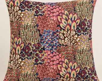 May include: A square throw pillow featuring a dense, repeating pattern of stylized botanical and fan-shaped motifs in shades of deep navy blue, magenta, soft pink, olive green, and golden yellow, set against a dark, textured fabric background.