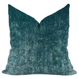 May include: A square decorative pillow with a teal and white textured design. The pillow has a soft, faded appearance, with a gradient effect from dark teal to a lighter shade. The pillow's fabric has a subtle, mottled pattern.