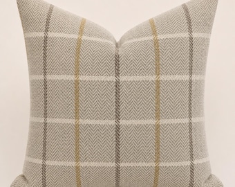 May include: A square throw pillow featuring a light beige and gray herringbone weave pattern. The fabric is decorated with a grid of vertical and horizontal stripes in muted gold and dark gray, creating a structured plaid design across the surface.