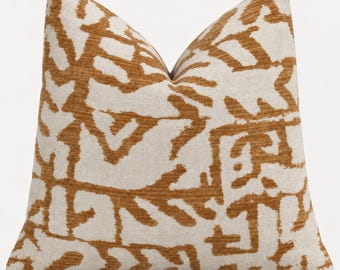 May include: A square throw pillow featuring a cream-colored base with a bold, abstract, burnt orange pattern. The design consists of irregular, interconnected shapes and lines that create a textured, organic appearance across the entire surface.