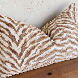 May include: A rectangular throw pillow featuring a textured, raised pattern of wavy, organic lines in shades of tan and brown against a cream-colored background. The fabric has a distinct, tactile surface with a repeating abstract design.