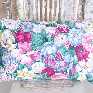 Puede incluir: Una almohada floral con una variedad de flores rosas, moradas, azules y amarillas sobre un fondo verde.