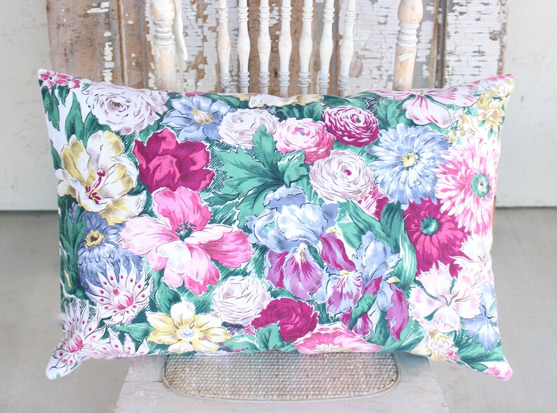 Puede incluir: Una almohada floral con una variedad de flores rosas, moradas, azules y amarillas sobre un fondo verde.