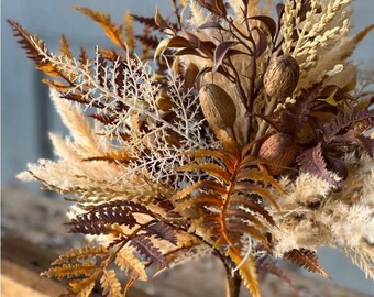 May include: A decorative floral arrangement featuring dried pampas grass, brown and orange fern fronds, and small oval seed pods. The bouquet includes various textures of dried foliage in shades of cream, tan, rust, and dark brown, gathered together on a single stem.