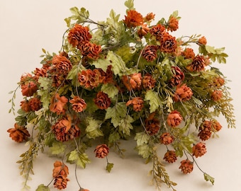 May include: A decorative floral arrangement featuring numerous small, rust-orange, cone-shaped blossoms interspersed with abundant, textured, light green foliage. The stems are thin and flexible, creating a cascading, rounded, and dense cluster.