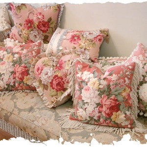 May include: A collection of floral patterned throw pillows with fringe trim. The pillows are arranged on a white wicker couch with a floral patterned fabric.