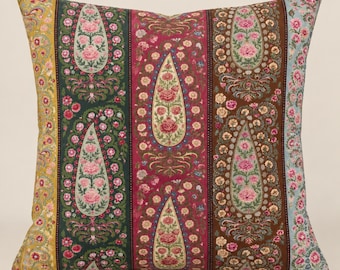 May include: A square throw pillow featuring a vertical striped pattern with paisley and floral motifs. The design includes bands of yellow, dark green, deep magenta, brown, and light blue, all decorated with intricate pink and cream flower prints.