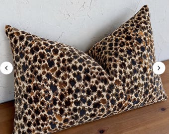 May include: A rectangular throw pillow featuring a dense, multi-tonal leopard print pattern in shades of dark brown, black, and tan. The fabric has a soft, textured appearance with a repeating spotted design covering the entire front surface.