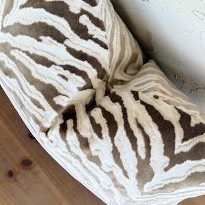 May include: A brown and white zebra patterned throw pillow. The pillow is made of a soft, plush fabric.