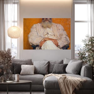 May include: A living room scene featuring a large gray sectional sofa with multiple pillows and a beige throw blanket. A round coffee table sits in front of the sofa. A painting of a man in white robes hangs on the wall.