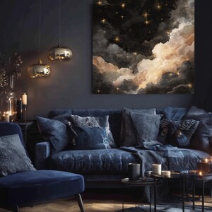 K&ouml;nnte beinhalten: Ein gro&szlig;er Leinwanddruck, der eine Nachthimmel-Szene mit dunklen Wolken, goldenen Sternen und warmem, leuchtendem Licht zeigt. Das Kunstwerk h&auml;ngt &uuml;ber einem marineblauen Sofa mit dekorativen Kissen und schafft eine gem&uuml;tliche und elegante Wohnzimmeratmosph&auml;re.