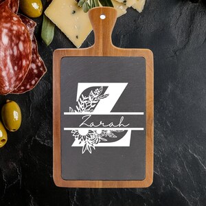 May include: A wooden serving board with a dark gray slate center. The slate is decorated with a white floral design and the letter "Z" with the name "Zarah" in script. The board has a handle.