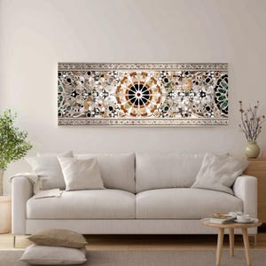 Op de afbeelding: Een lang, rechthoekig kunstwerk voor aan de muur met een gedetailleerd moza&iuml;ekontwerp. Het moza&iuml;ek heeft een centraal cirkelvormig patroon in bruin en zwart, omgeven door ingewikkelde bloemen en geometrische elementen in verschillende kleuren. Het kunstwerk is omlijst met een zilveren rand en hangt boven een witte bank.