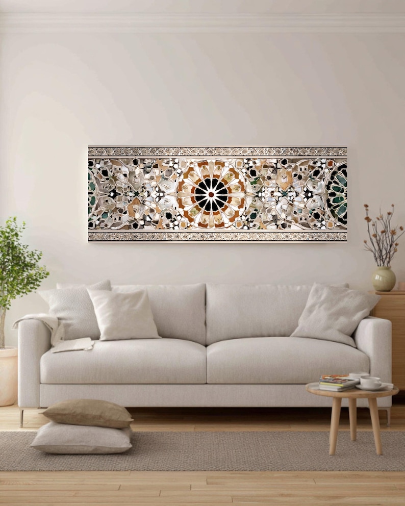 Op de afbeelding: Een lang, rechthoekig kunstwerk voor aan de muur met een gedetailleerd moza&iuml;ekontwerp. Het moza&iuml;ek heeft een centraal cirkelvormig patroon in bruin en zwart, omgeven door ingewikkelde bloemen en geometrische elementen in verschillende kleuren. Het kunstwerk is omlijst met een zilveren rand en hangt boven een witte bank.