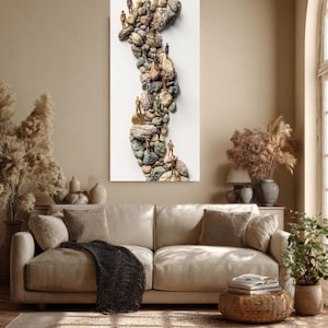 May include: A vertical art piece featuring a winding path of stones with miniature figures. The artwork is set against a white background, with a neutral-toned living room setting. The figures are in various poses, suggesting movement along the stone path.