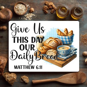 Może przedstawiać: Dekoracyjna deska do krojenia z napisem "Give Us This Day Our Daily Bread, Matthew 6:11." Obraz przedstawia ilustracje chleba, miski zupy i niebiesko-białego kosza w kratkę. Tło zawiera składniki takie jak owies, orzechy włoskie i olej.