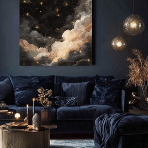 K&ouml;nnte beinhalten: Ein gro&szlig;es quadratisches Leinwandkunstwerk, das einen Nachthimmel mit Wolken und Sternen darstellt. Das Kunstwerk zeigt einen dunklen Hintergrund mit flauschigen, hellfarbigen Wolken und funkelnden goldenen Sternen. Der Raum hat ein dunkelblaues Sofa, einen Couchtisch und dekorative Beleuchtung.
