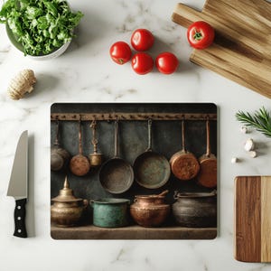 May include: A kitchen-themed image featuring a cutting board with hanging antique cookware. Red tomatoes, a bowl of greens, a mushroom, a knife, and wooden cutting boards are also present. The cookware includes pots, pans, and ladles in various sizes and materials.