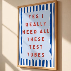May include: A framed wall art print featuring a light blue wavy-edged rectangle centered on a background of vertical dark blue stripes. The text in red capital letters reads: YES I REALLY NEED ALL THESE TEST TUBES. The frame is light wood.