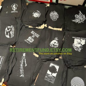 Może przedstawiać: Kolekcja czarnych łat z tkaniny z białymi wzorami. Łaty przedstawiają r&oacute;żne hasła i obrazy, w tym "Ratuj Ziemię", "Zostaw mnie w spokoju", "Czytaj więcej książek" i "Nie bierz nic, zostaw wszystko".