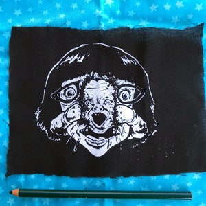 May include: Black and white patch with a graphic of a person with a bowl haircut wearing glasses and a creepy expression. The person's face is distorted and appears to have a second face inside of it.