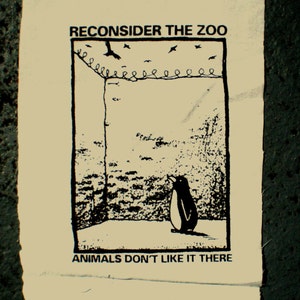 Puede incluir: Ilustración en blanco y negro de un pingüino mirando hacia arriba a una valla con pájaros volando por encima. El texto "RECONSIDER THE ZOO" y "ANIMALS DON'T LIKE IT THERE" está impreso debajo de la imagen.