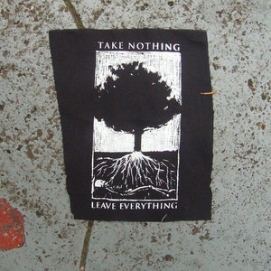 May include: Black patch with a white illustration of a tree and its roots. The text "TAKE NOTHING" is above the tree, and "LEAVE EVERYTHING" is below. The patch is rectangular with slightly frayed edges.
